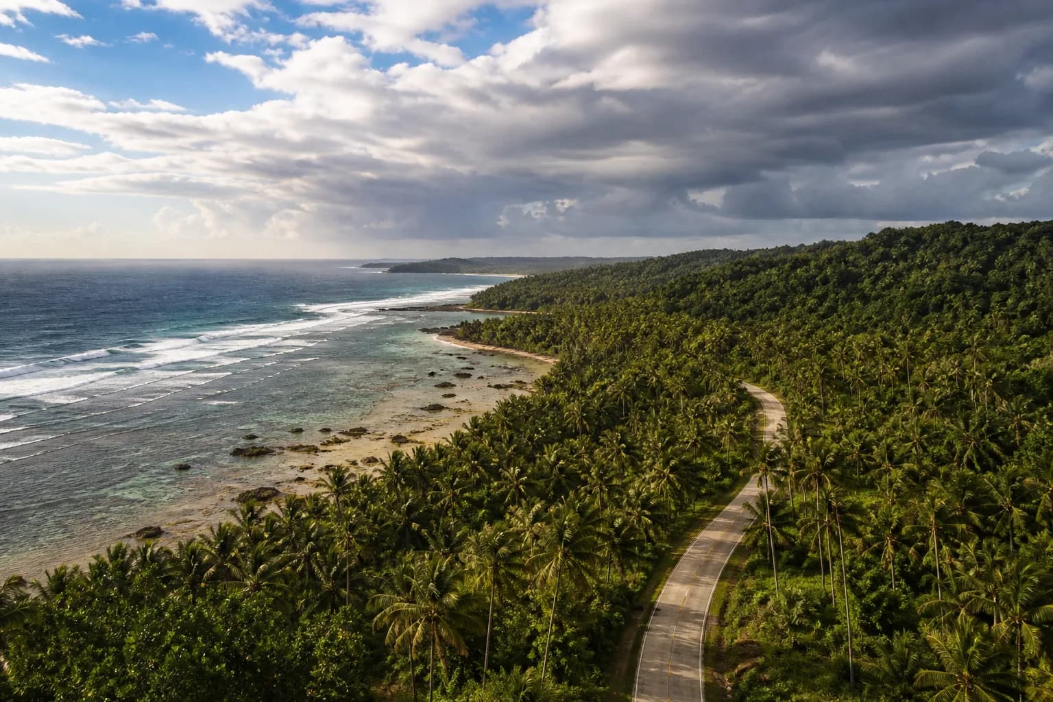 A long coastal road through Siargao beneath mixed sun and cloud